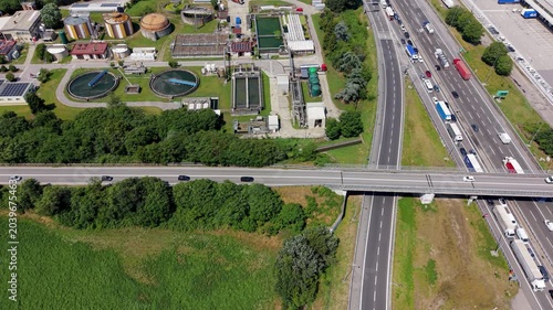 Wastewater Treatment Plant Adjacent to Highway: An aerial view showcasing a functional wastewater treatment plant with circular clarifiers and industrial buildings. Italy, Milan