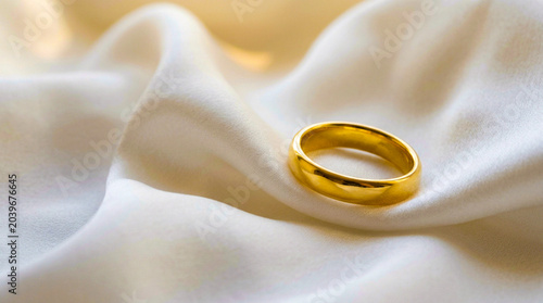 Simple polished gold ring resting on soft white silk with precious, accessory