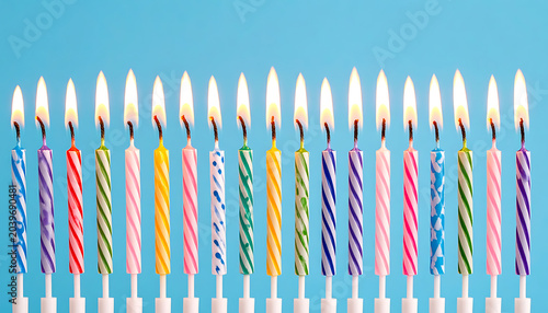 Row of colorful birthday candles lit and burning against a clear blue background, party celebration element