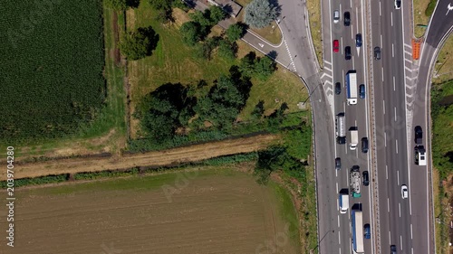 Aerial Highway View: Cars and trucks travel on a busy highway from an aerial perspective, bordered by agricultural fields and green trees.