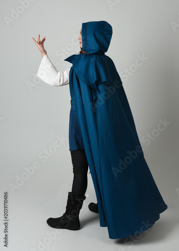 full length portrait of model wearing medieval fantasy warrior historical costume with blue hooded cloak. silhouette figure,  walking away in back view on studio background.