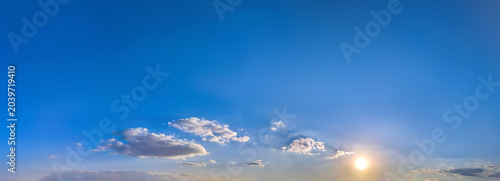 Tableau sur toile Expansive sky where a low sun gilds scattered clouds, blue deepening toward zenith softening along horizon