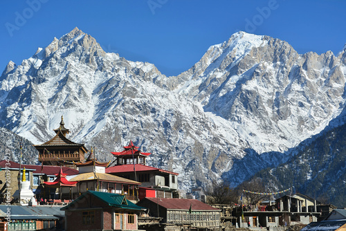Vibrant village scene in Kalpa, Himachal Pradesh, where colorful temple roofs contrast with massive, rugged snow-covered peaks related to cultural heritage amidst majestic natural unique landscapes