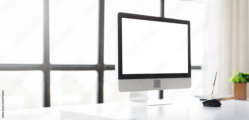 Fototapeta premium Modern computer display with a blank white screen on a sleek desk, providing ample copy space for creative mockups, showcasing a bright and minimalist workplace