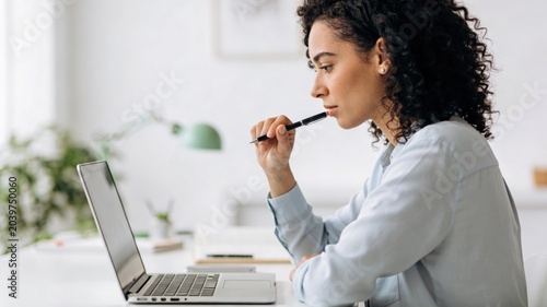 Professional woman pauses to think while using laptop at her desk
