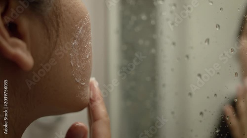 Close-Up Shot of a Person Applying Skincare Cream to Their Face in a Steamy Bathroom Mirror