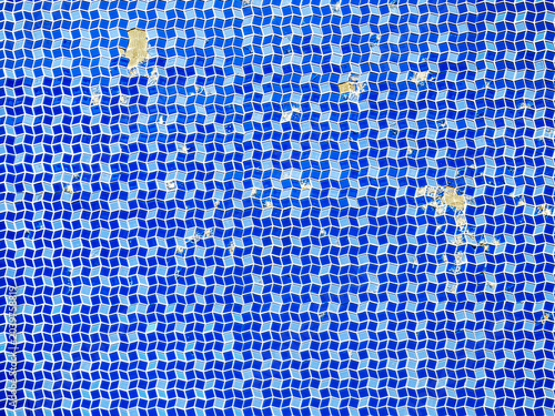 Blue mosaic abstract background with tiles falling off in places. Small geometric ceramic blue, light blue and white tiles create a nice wavy pattern.