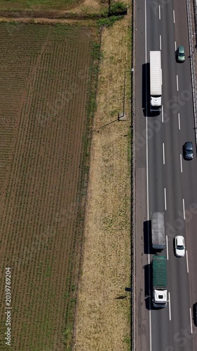 Aerial Highway A50 Traffic: A high-angle view captures the bustling activity on a multi-lane highway, with various vehicles including trucks and cars moving along the road. Italy, Milan