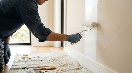 Professional painter wearing grey gloves using a paint roller to apply fresh white coat on an interior residential wall during a home renovation project
