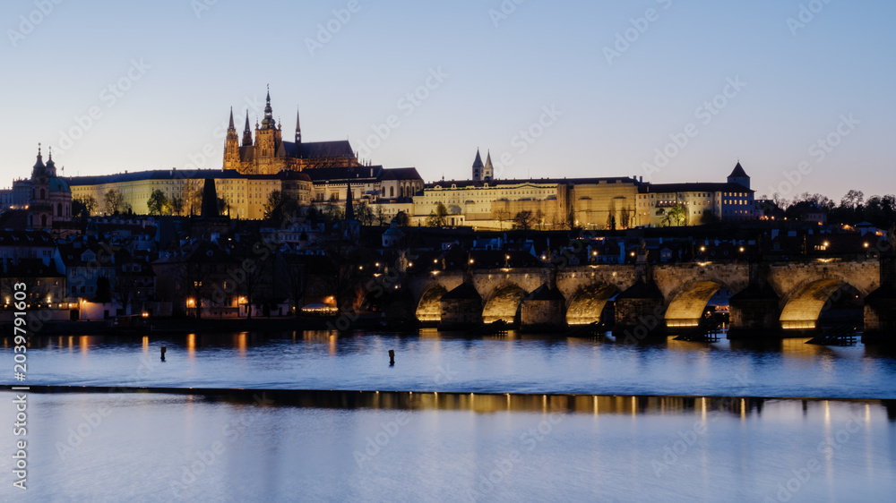 Obraz premium Evening lights illuminate Pragues majestic castle and Charles Bridge along the Vltava River