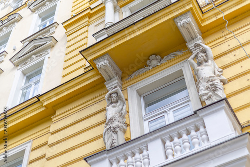 Εκτύπωση καμβά Ornate historical building facade with yellow stucco, white balcony balustrade, and classical caryatid statue sculptures in Prague, Czech Republic
