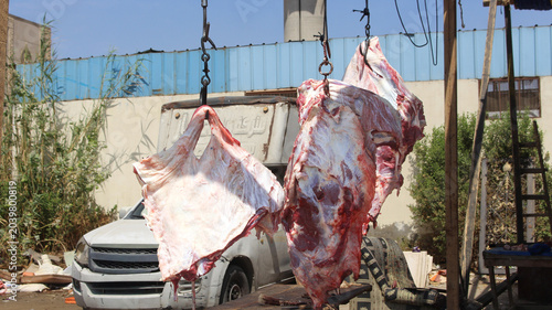 Cuadro en lienzo Fresh meat carcasses hanging on metal hooks inside a butcher processing facility and food production environment