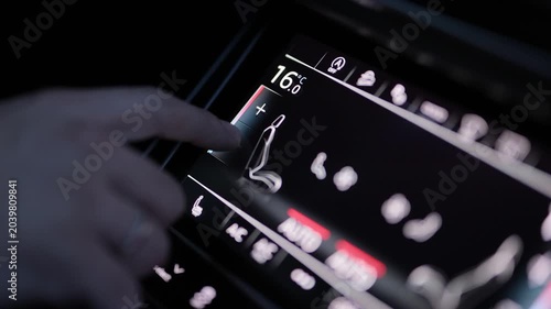 A hand adjusts the climate control system in a car. Male hand regulating the air conditioning control in a car. The warm glow of the controls shows the set temperature