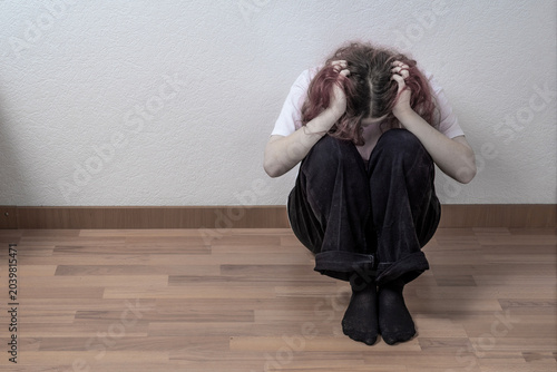 Woman sitting on the floor with head down and arms around knees, concept of depression, anxiety and loneliness, mental health crisis and psychological distress indoors.