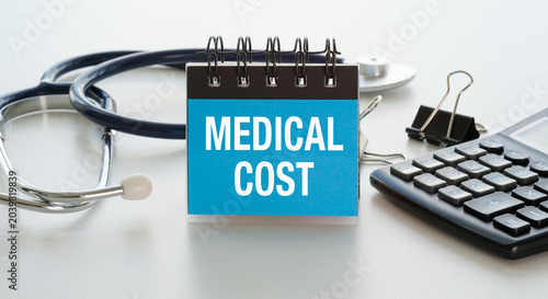 Medical cost sign sits beside stethoscope and calculator. Table surface holds office tools in clean arrangement.
