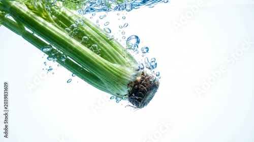Vibrant green celery stalks plunging into clean, clear water, creating refreshing bubbles on a bright white background.