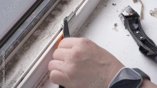 Removing Old Sealant from Window Frame during Renovation. The girl removes the old sealant from the window frame.