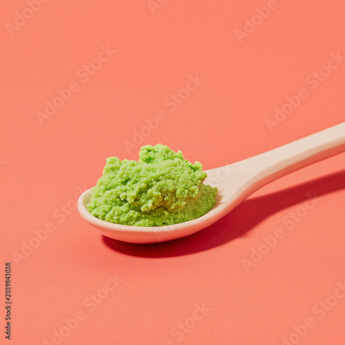 A spoon with bright green wasabi paste against a peach background