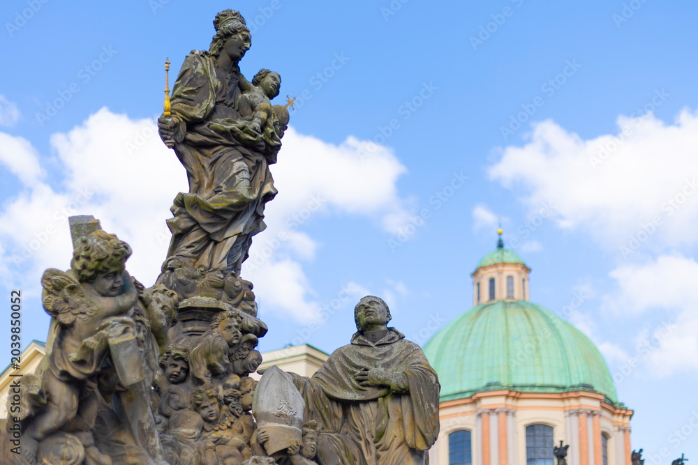 Obraz premium Historic baroque statue of Madonna and Saint Bernard on Charles Bridge with Saint Francis dome in Prague, Czech Republic.