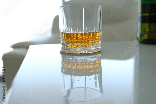 a glass of whiskey on a white table. a glass of whiskey is reflected in a white glass table. alcohol drinks concept