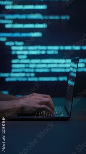 Close up of programmer hands typing on laptop keyboard in dark workspace with blue code lines in background. Coding process and software development or cybersecurity concept. Vertical video