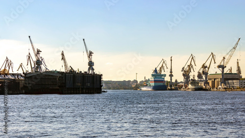 Tableau sur toile Saint Petersburg, Russia: Wide view from Blagoveshchensky Bridge to Baltic Shipyard with cranes, dockyards and cargo vessel on Neva River