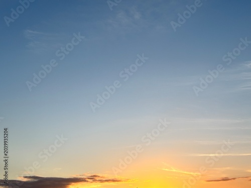 Beautiful twilight sky gradient background. Clear blue sky transitioning into vibrant orange and yellow at the horizon with soft clouds and copy space.