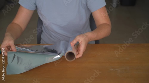 Woman unrolling aluminum foil and cutting a piece with scissors at a table, high quality audio recording. Crisp cutting and metallic rustling sounds. Kitchen task, food prep and everyday lifestyle