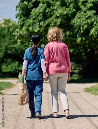 Nurse caregiver with senior woman walking outdoors and helping with shopping bag with groceries