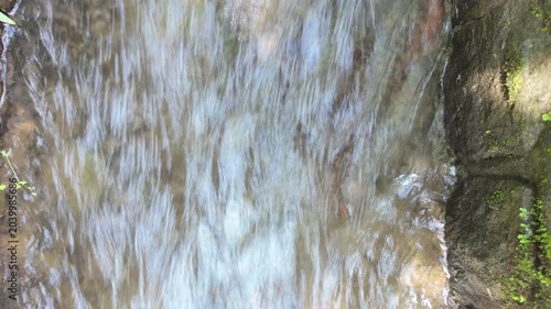 A tranquil stream of water flowing gently over smooth stones surrounded by lush greenery creating a peaceful outdoor atmosphere