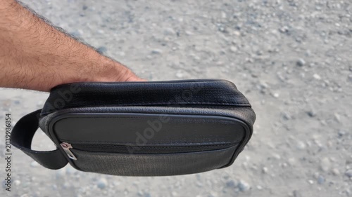 Black PU leather men’s clutch with wristlet strap and zippered pocket outdoors in nature.