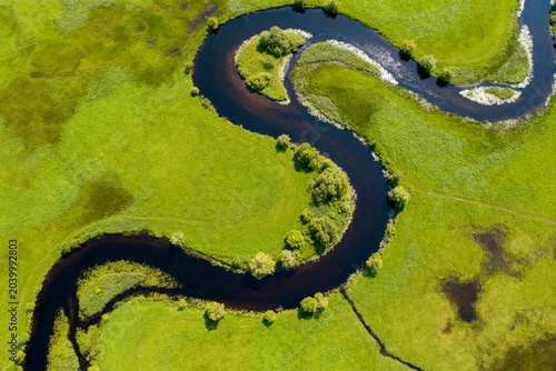 Aerial view of winding river through green grassland with scattered trees