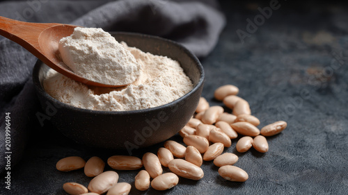 White bean flour wooden spoon black bowl dry white beans rustic kitchen healthy ingredient plant based protein natural food close up textured background