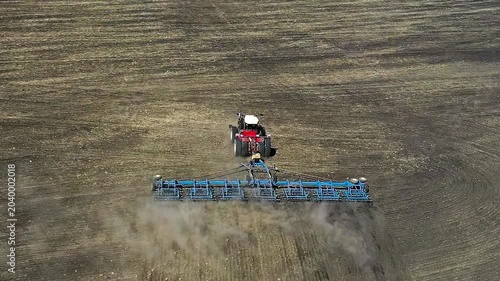 Enjoy an aerial view of a bold red tractor plowing a sprawling field. The dust trails behind, painting a picture of hard work and dedication etched into the landscape. Aerial FHD footage.