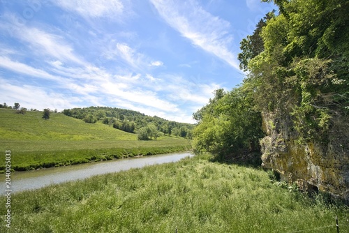 Wispy white clouds in a blue sky float about a small creek in a lush green valley on a spring morning in Dubuque County, Iowa.