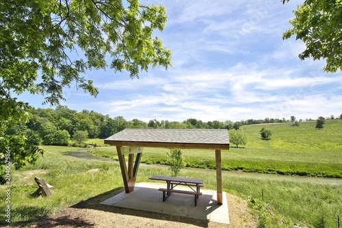 View of a bench and picnic shelter overlooking a small stream in a lush green valley on a morning in May along the Heritage Trail in Dubuque County, Iowa.