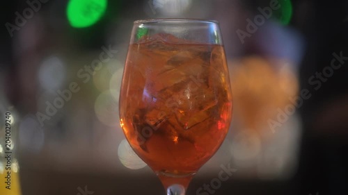 An aperol spritz drink on a glass at a lively bar during the evening with defocused background with a barman dancing