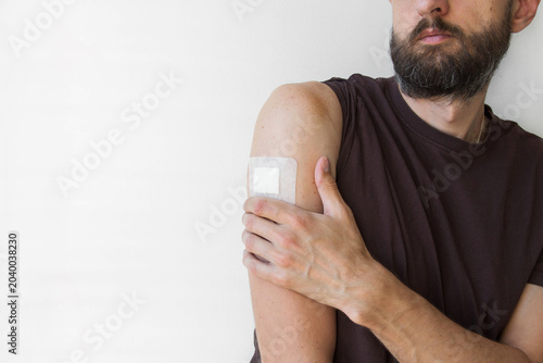Medical adhesive bandage on upper arm of bearded adult man, closeup after minor medical procedure, injection, vaccination or mole removal, healthcare recovery, wound care, dermatology treatment 