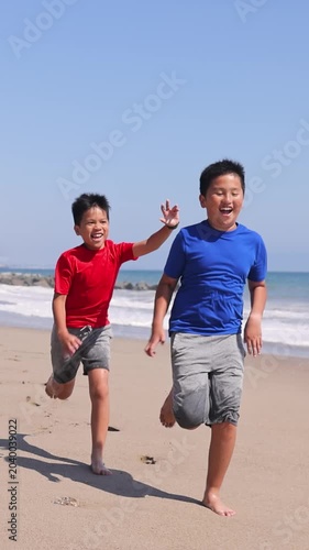 Two brothers playing tag on the beach in Santa Monica. Slow Motion. Vertical video.