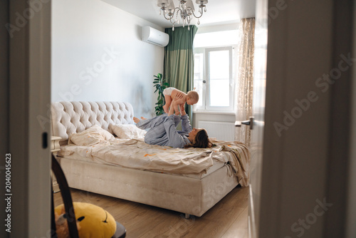 Joyful mother playing with her little baby on bed in the morning