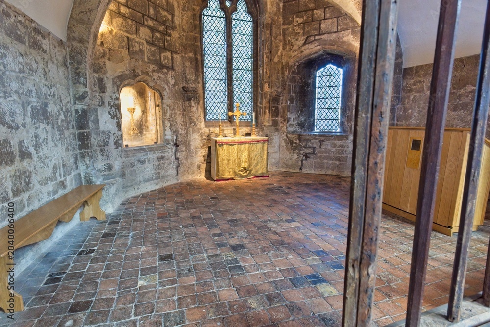 Fototapeta premium A stone room with a small wooden altar, large arched windows, and a patterned brick floor at Gloucester Cathedral - Gloucester - Gloucestershire - UK