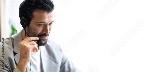 Attractive business man in suits and headsets smiling while working on desktop computer at modern office desk . Customer service assistant working in office. VOIP Helpdesk headset