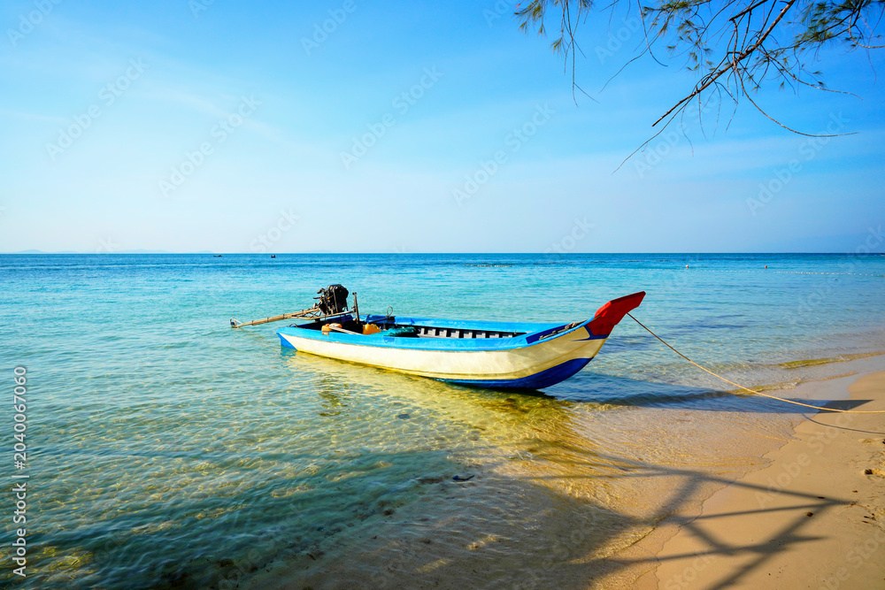 Obraz premium Fishing boat in turquoise sea water on sunny day near coastline in tropical Phu Quoc island in Vietnam. Traditional Thai long-tail boat in shallow water near shore with crystal clear sea