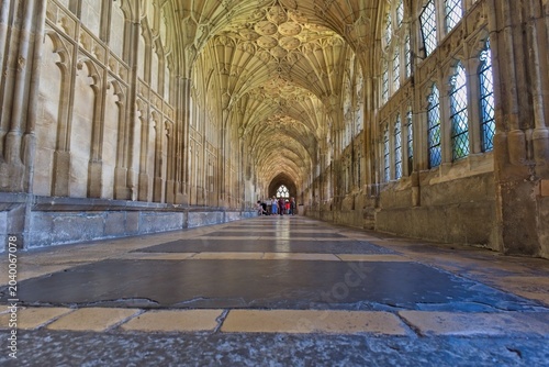 Bild auf Leinwand A long, grand stone corridor features an ornate vaulted ceiling and arched windo