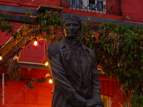 Foto Estatua de bronce de personaje histórico frente a una colorida fachada roja con