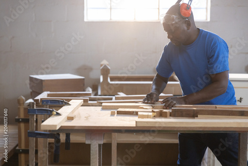 Carpenter shaping wooden plank on workbench with metal clamps in carpentry shop, with natural light