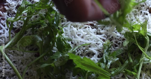Arugula leaves sprinkled over beef covered with grated hard cheese, carpaccio preparing, close up