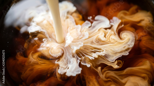 Creamy milk or creamer pouring into dark black coffee creating dynamic abstract swirling textures waves and cloud patterns close up overhead macro shot
