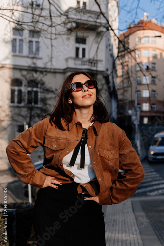 Beautiful young woman enjoying a sunset in Prague city. Stylish girl in a fashionable outfit posing outdoors near historic architecture in warm golden light. Urban fashion and lifestyle concept.