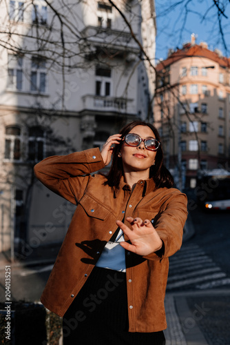 Beautiful young woman enjoying a sunset in Prague city. Stylish girl in a fashionable outfit posing outdoors near historic architecture in warm golden light. Urban fashion and lifestyle concept.